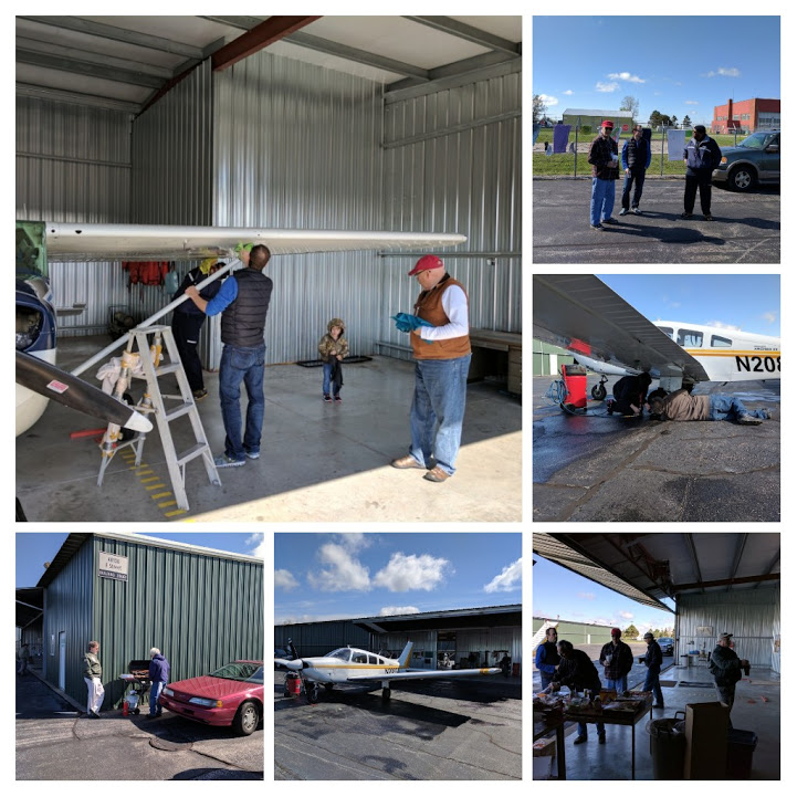 People washing planes, barbequeuing, and chatting near the hangars on a summer day with blue skies.